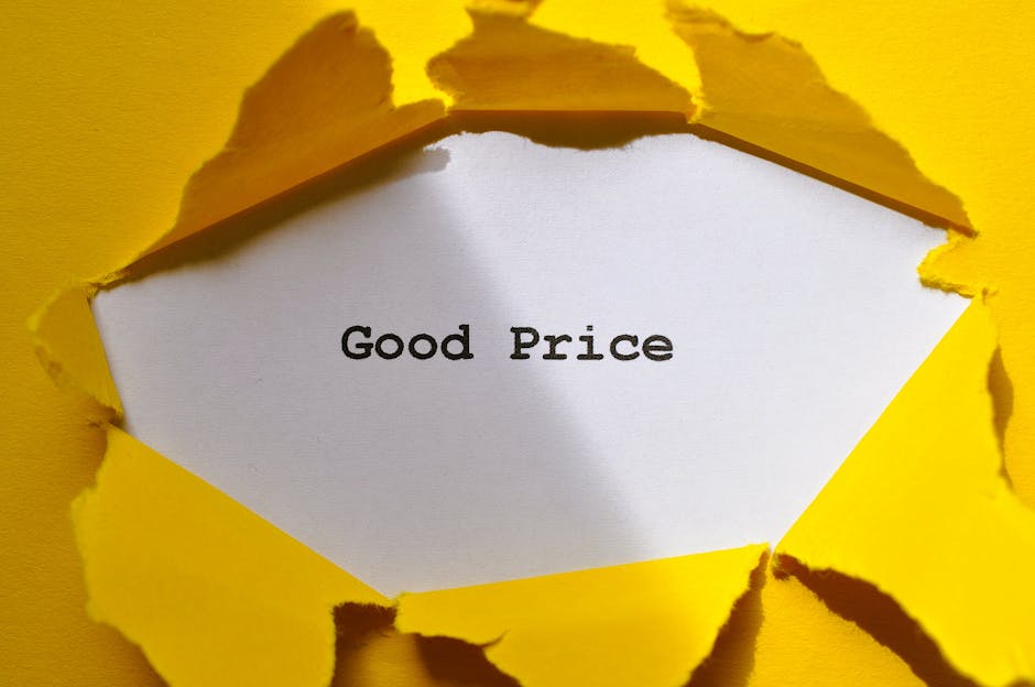 A white rectangular sheet of paper with the words 'Good Price' printed in black ink, partially torn from bright yellow paper or cardboard. The torn edges reveal rough, irregular cuts surrounding the white paper. The background consists of the yellow material, which appears to be part of a packaging or decorative surface. The tearing creates a jagged, irregular frame around the message, emphasizing the text in the center. The lighting is even, with no shadows, and the focus is sharp on the torn edges and printed message, suitable for illustrating themes related to pricing, value, or negotiations in the context of home relocations or moving services provided by Man With a Van Hornsey.